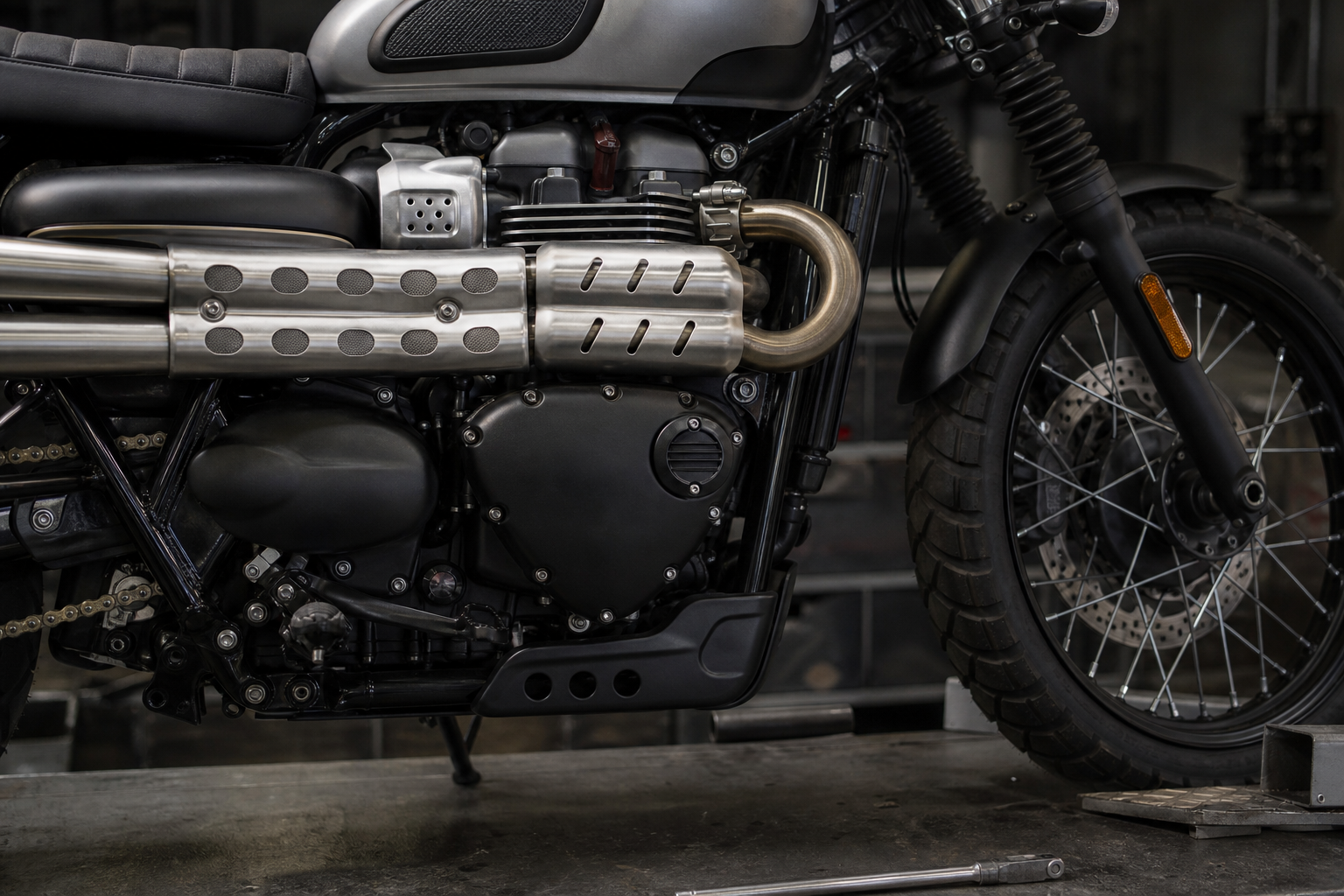 Triumph Scrambler 900 900cc Bonneville twin high exhaust brake fork and tire detail in an industrial inspection bay